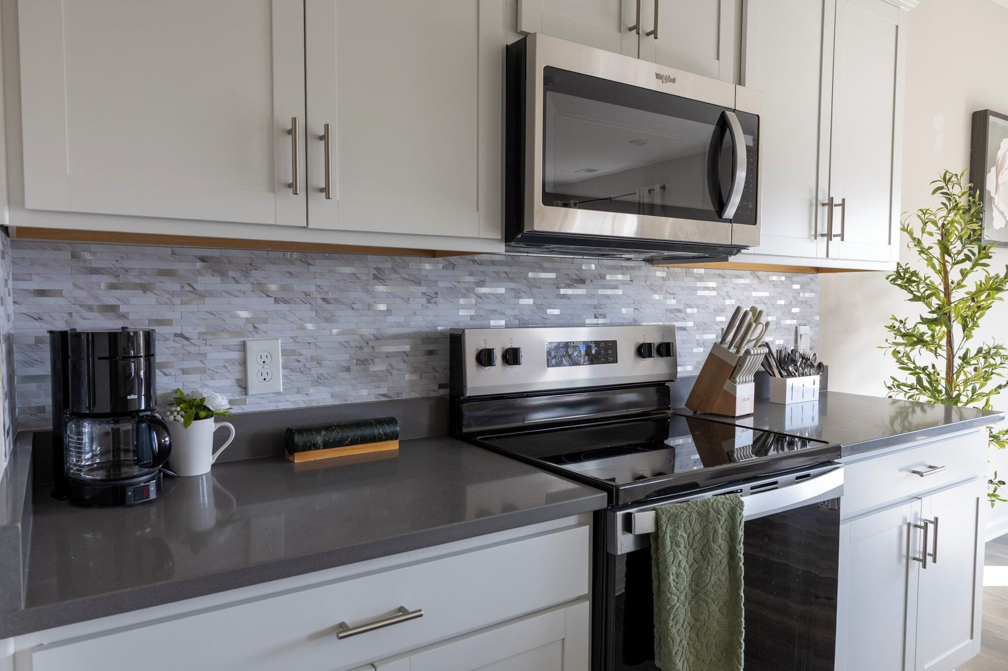 A modern kitchen with white cabinets, a stainless steel microwave, a black stove, and a marble backsplash.