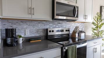 A modern kitchen with white cabinets, a stainless steel microwave, a black stove, and a marble backsplash.
