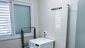 Un baño moderno y funcional con lavadora integrada, un lavamanos pequeño y una ventana con persianas.