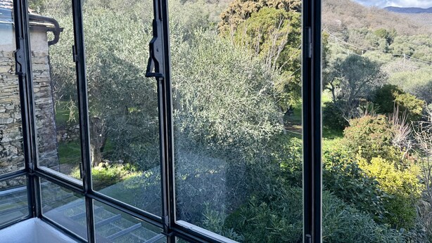 A room with large windows offering a view of a lush garden and distant hills. - Relais Limone (Dolcedo)