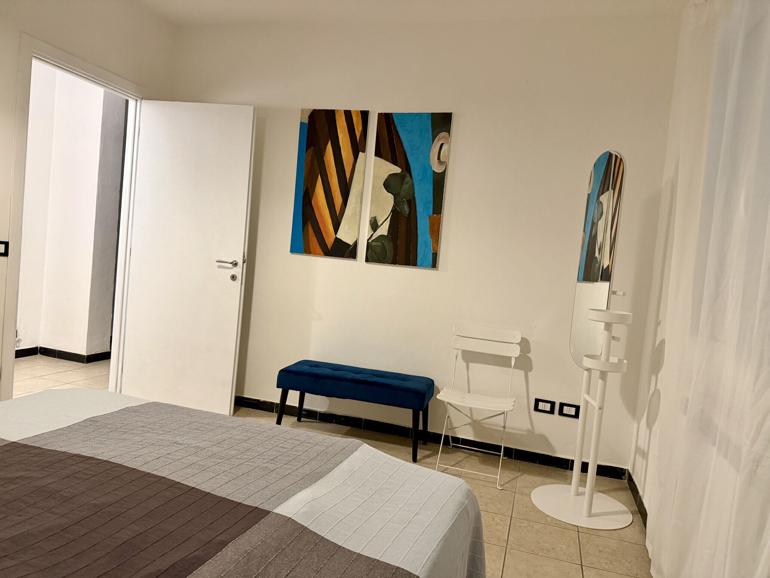 A bedroom with a bed, a bench, a chair, and a wall-mounted lamp.