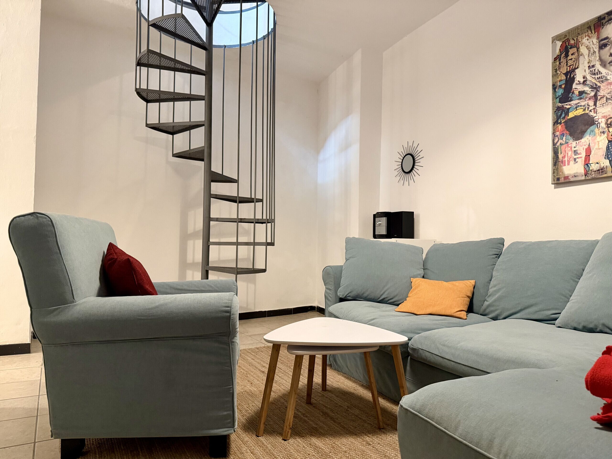 Ein modernes Wohnzimmer mit einem grauen Sofa, einem kleinen Couchtisch und einer Wendeltreppe.