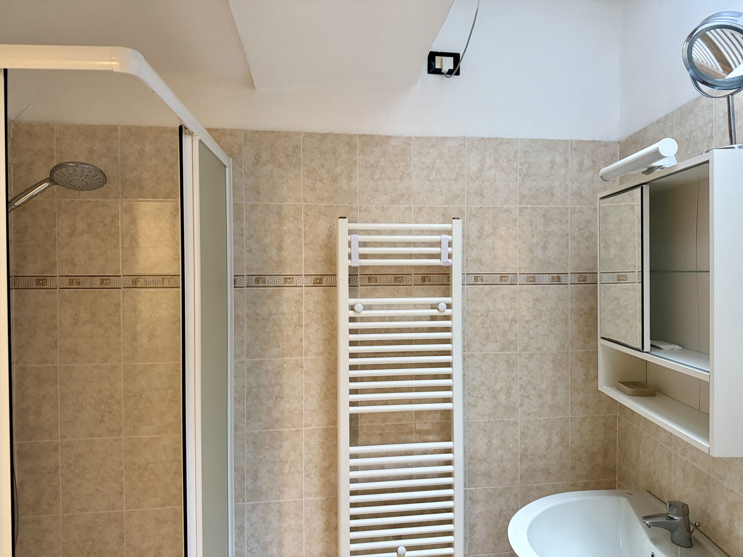 Baño con ducha, toallero, lavamanos y espejo.
