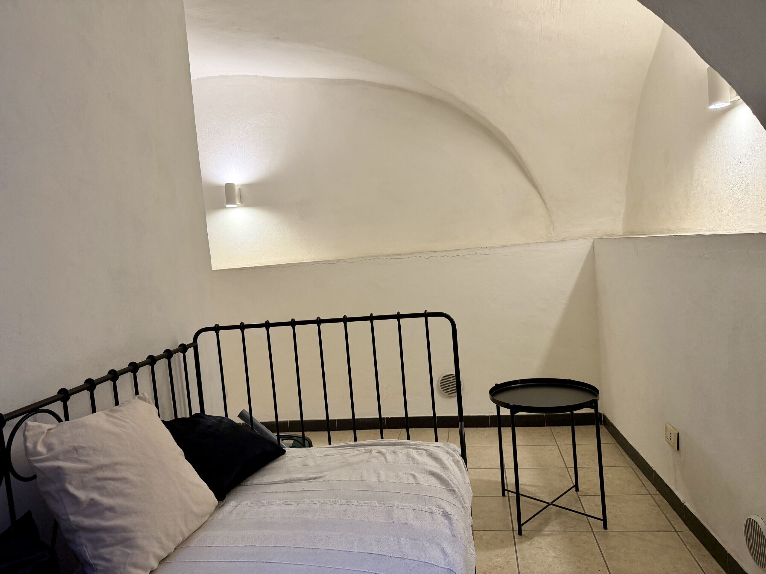 A small, dimly lit room with a single bed, a small table, and a slanted ceiling.