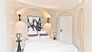 Une chambre moderne avec un grand lit, deux tables de chevet, une porte blanche et un tableau abstrait noir accroché au mur.