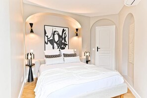 A modern bedroom with a large bed, two bedside tables, a white door, and a black abstract painting on the wall. - Design & bright apartment, Victor Hugo (Paris)