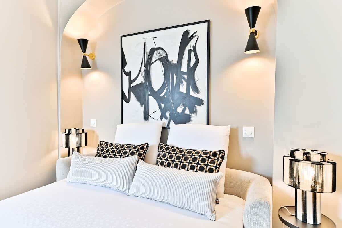Une chambre moderne avec un grand lit, deux appliques murales décoratives et une œuvre d’art abstraite accrochée au-dessus du lit.