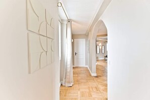 A hallway with a wooden floor, white walls, and a door at the end. - Design & bright apartment, Victor Hugo (Paris)