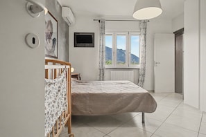 A bedroom with a bed, a TV, a window with curtains, and a radiator.