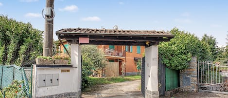 A gated entrance with a pergola, a utility pole, and a building with a tiled roof.