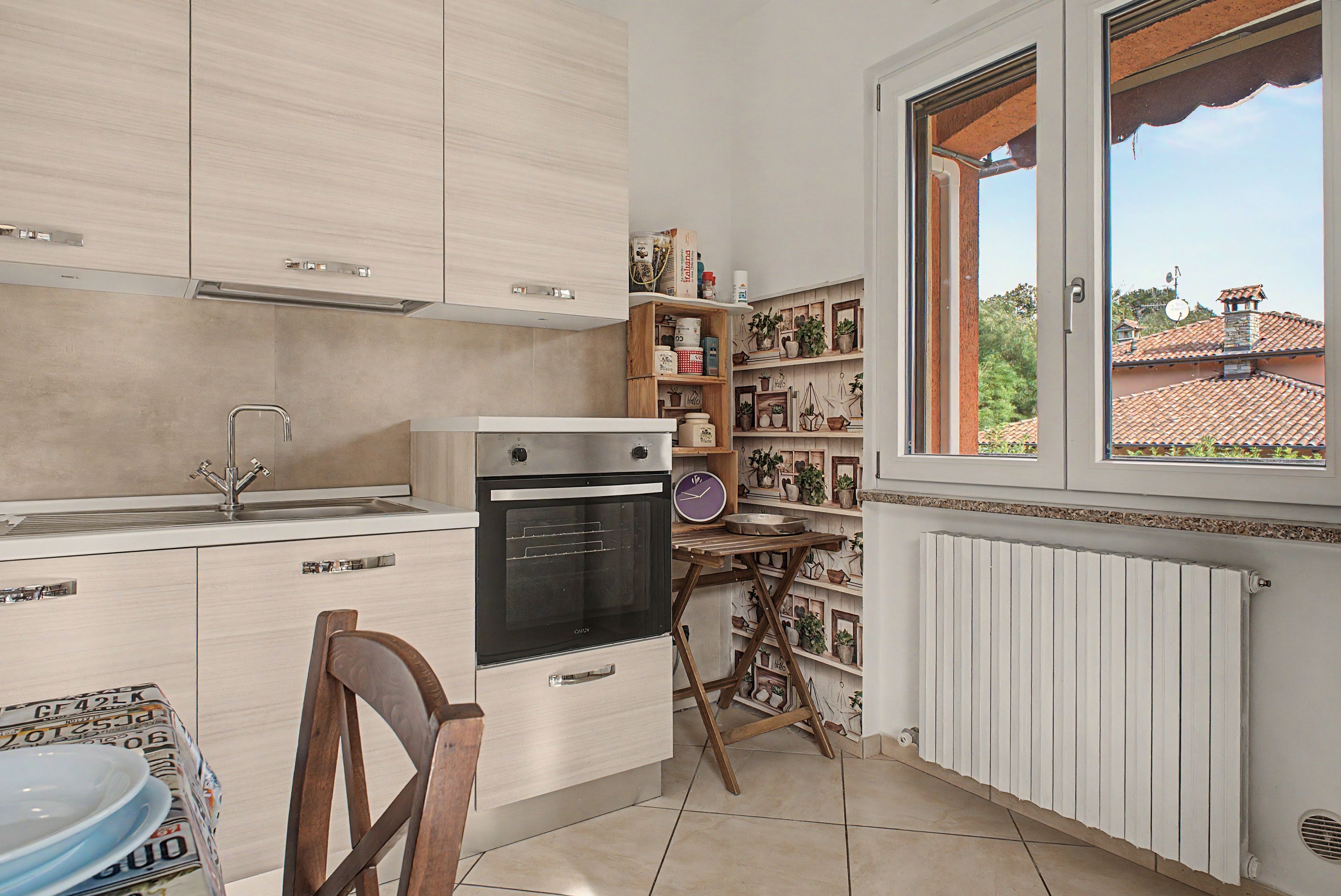 A compact kitchen with a built-in oven, a sink, and a window overlooking a residential area.