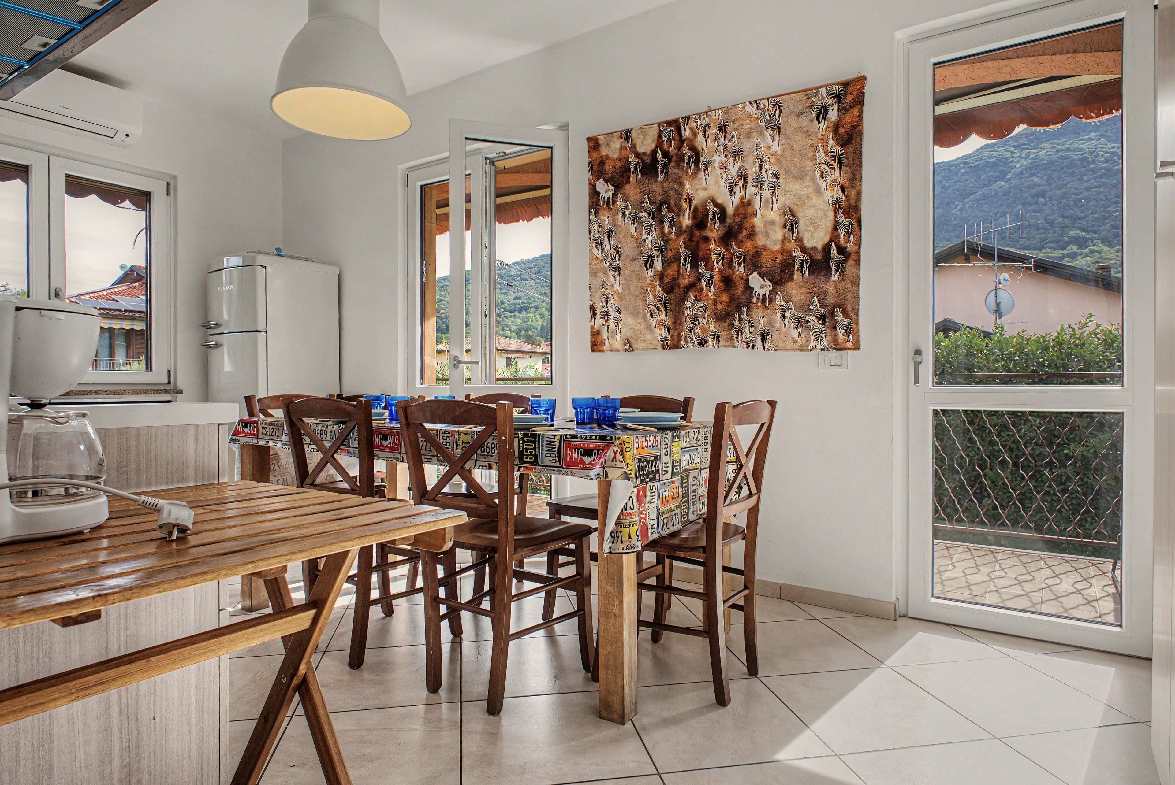 Un coin repas avec une table et des chaises, un réfrigérateur, un tableau représentant une zèbre accroché au mur, et une vue sur l’extérieur grâce à une porte vitrée.