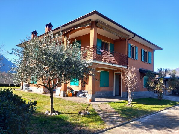 Ein zweistöckiges Haus mit Balkon, ein kleiner Baum im Vorgarten und ein klarer Himmel.
