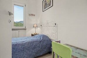 Ein Schlafzimmer mit einem Bett, einem Nachttisch, einer Lampe, einem Fenster mit Blick und einem gerahmten Bild an der Wand.