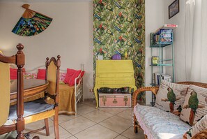 A room with a wooden bed, a yellow dresser, a green wall with a tropical pattern, and a bookshelf with books and a board game. - Apartment 'Sunset On Lake Maggiore 2 Garages' with Garden, Balcony and Wi-Fi (Porto Valtravaglia)