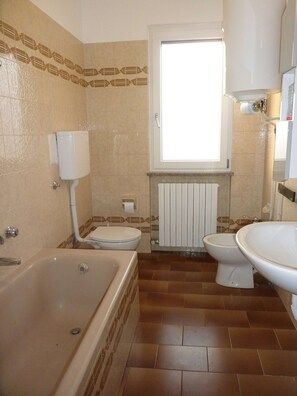 Ein Badezimmer mit einer Badewanne, zwei Toiletten, einem Fenster und einer Heizung.