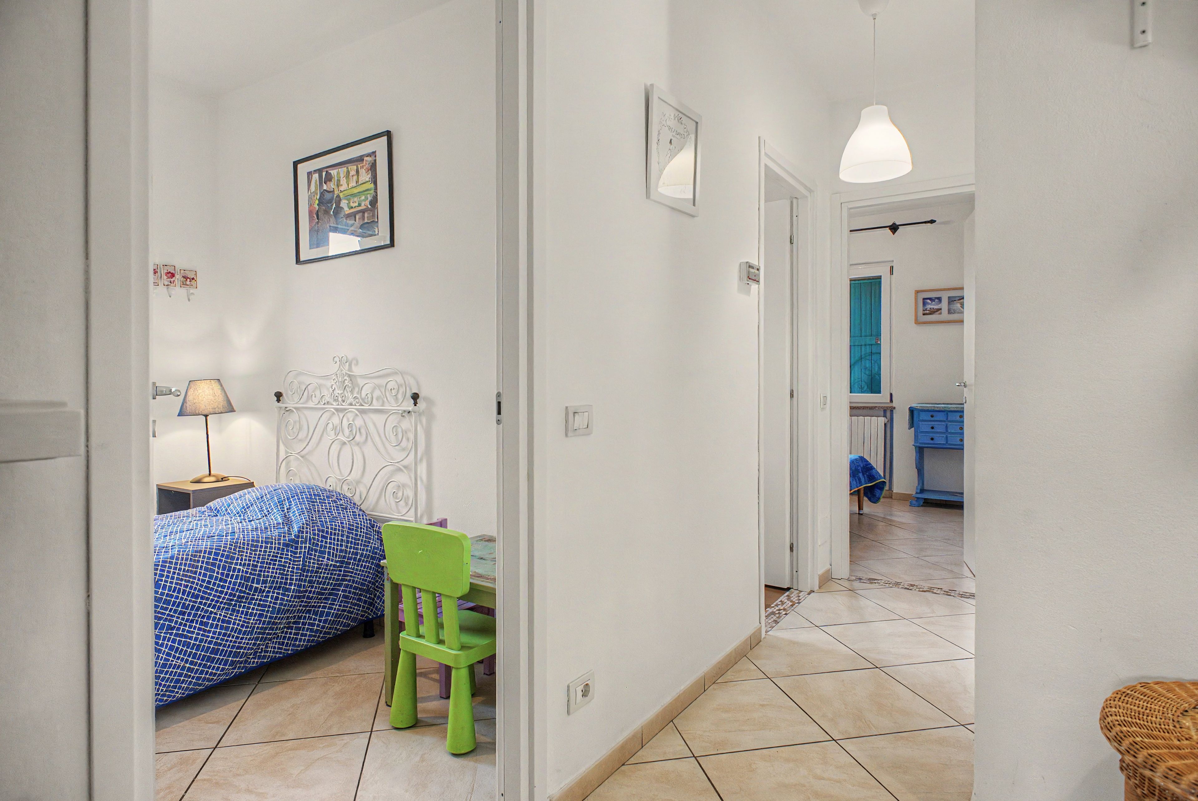 Une chambre à coucher avec un lit, une chaise, une table de chevet et une lampe. Une porte donne accès à une autre pièce.