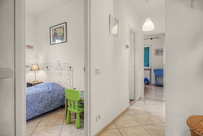 A bedroom with a bed, a chair, a bedside table, and a lamp. There is a door leading to another room. - Apartment 'Sunset On Lake Maggiore 2 Garages' with Garden, Balcony and Wi-Fi (Porto Valtravaglia)