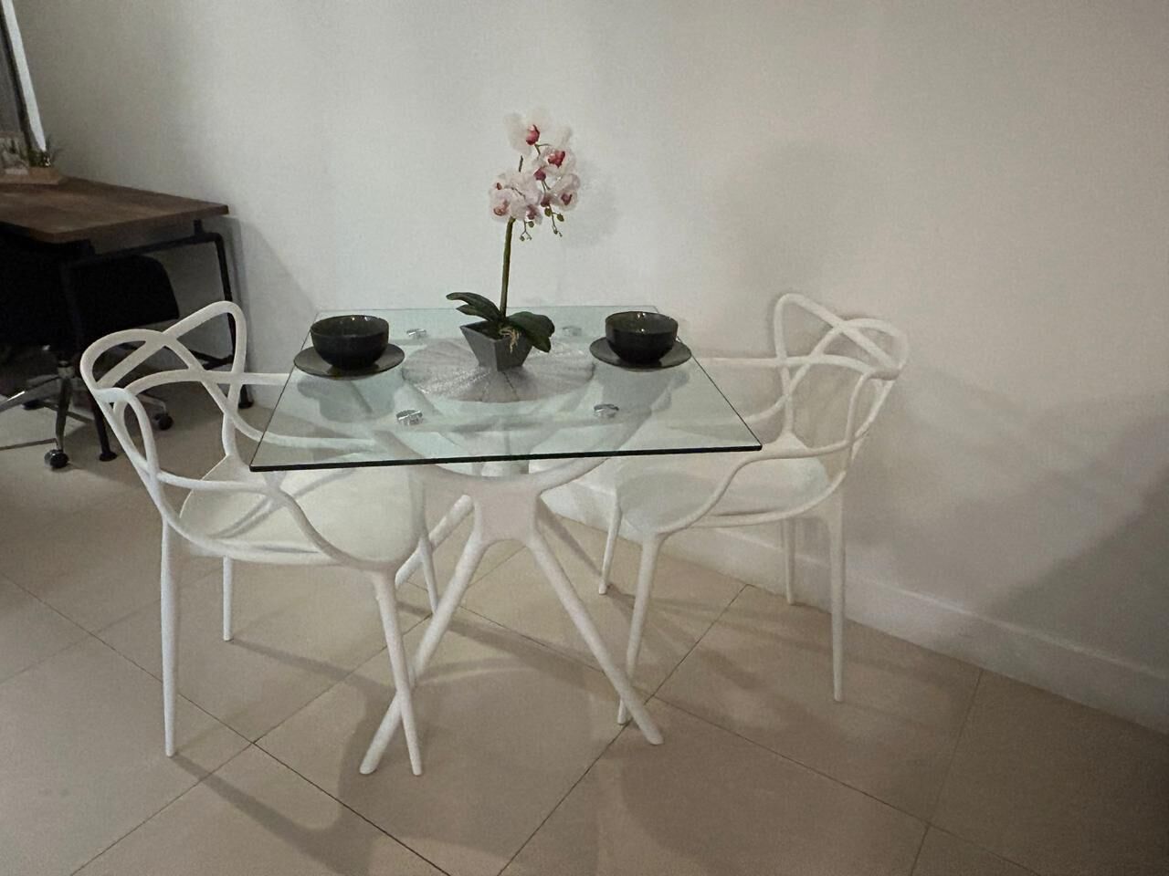 A glass-top dining table with four white chairs, a potted orchid, and two black bowls.