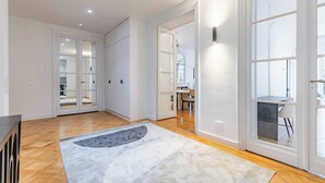 A spacious room with a wooden floor, a grey rug, and a large window. - Appartement de prestige climatisé (Paris)