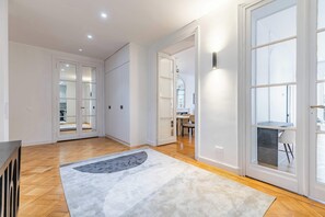 A spacious room with a wooden floor, a grey rug, and a large window. - Appartement de prestige climatisé (Paris)