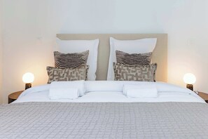 A neatly made bed with white linens and two pillows with a striped pattern. - Appartement de prestige climatisé (Paris)