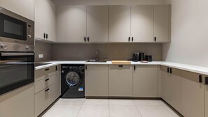 A modern kitchen with built-in appliances, including a microwave, oven, and dishwasher, and a sink with a wooden cutting board. - Appartement de prestige climatisé (Paris)