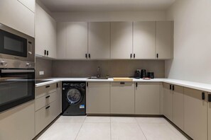 A modern kitchen with built-in appliances, including a microwave, oven, and dishwasher, and a sink with a wooden cutting board. - Appartement de prestige climatisé (Paris)