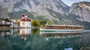Un bateau transportant des passagers, une église surmontée de coupoles rouges et, au loin, des montagnes.