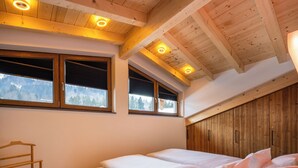 Une chambre avec un plafond en bois, deux fenêtres équipées de stores, un lit avec du linge de maison blanc et une armoire en bois.