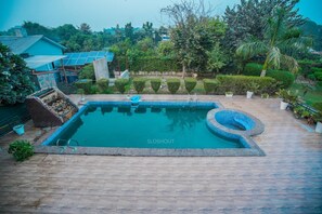 A swimming pool with a unique design, surrounded by a wooden deck and potted plants. - Taj Royal Farm (Noida)