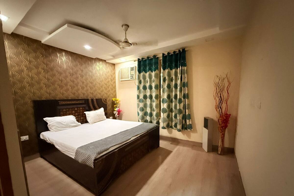 A hotel room with a large bed, a ceiling fan, and a window with patterned curtains.