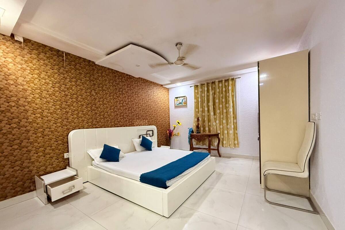 A modern hotel room with a large bed, a chair, a small table, and a ceiling fan.