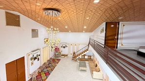 A spacious living area with a high wooden ceiling, a staircase, and a sofa set. - Taj Royal Farm (Noida)