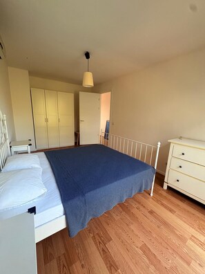 A bedroom with a bed, a dresser, a wardrobe, and a hanging light fixture.