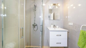 Een moderne badkamer met een glazen douchecabine, een wit aanrecht met een spiegel, en een groene handdoek aan de muur.