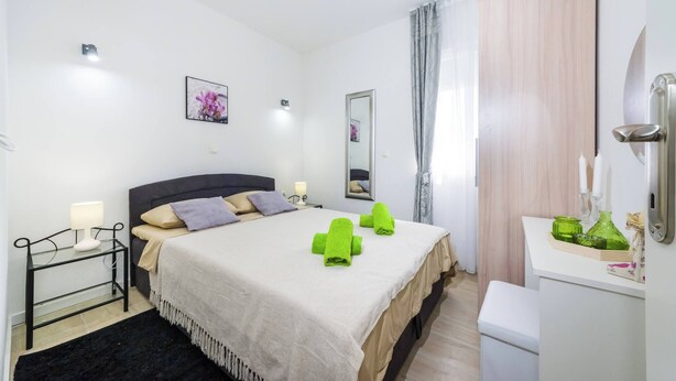 Een keurig opgemaakt slaapkamer met een bed, nachtkastjes, een spiegel en een klein badkamertje.