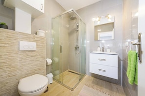 Ein modernes Badezimmer mit einer gläsernen Dusche, einer weißen Toilette, einem Waschtisch mit Spiegel und einem grünen Handtuch, das an der Wand hängt.