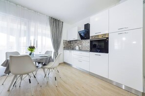 Eine moderne Küche mit weißen Schränken, einem eingebauten Backofen und einem Essbereich mit Tisch und Stühlen.