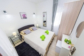 Ein Hotelzimmer mit Bett, Nachttisch, Lampe und einem kleinen Schreibtisch mit Spiegel und grünen Flaschen.