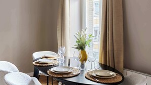 A dining table set with plates, glasses, and a vase with greenery, positioned near a window with curtains. - Marais — Confort moderne & charme parisien (Paris)