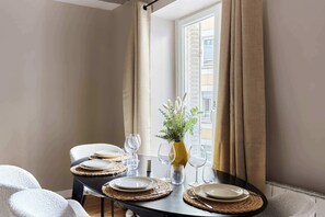 A dining table set with plates, glasses, and a vase with greenery, positioned near a window with curtains. - Marais — Confort moderne & charme parisien (Paris)