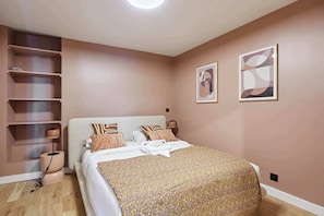 A bedroom with a bed, a bedside lamp, a shelf unit, and two wall-mounted artworks. - Marais — Confort moderne & charme parisien (Paris)