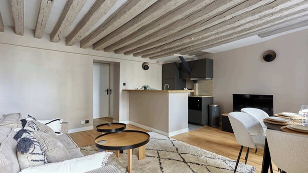 A modern living room with a sofa, coffee table, and a dining area with chairs and a table set for two. - Marais — Confort moderne & charme parisien (Paris)