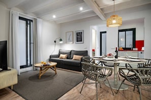 A modern living room with a sofa, coffee table, dining table, and chairs. There is a television, a lamp, and artwork on the walls. - Rustic-Chic Gracia Apartment Verdi Bajos (Barcelona)