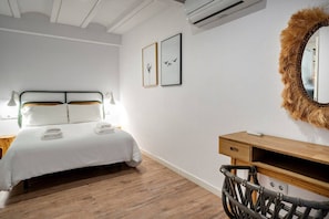 Una habitación de hotel con una cama, una mesita de noche de madera, un espejo con adornos de piel y dos cuadros en la pared.