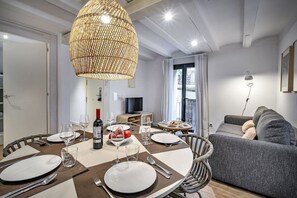 A dining area with a round table set for four, a bottle of wine, and a bowl of fruit. - Gracia Private Terrace Apartment Verdi Entresuelo (Barcelona)