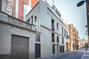 A street view with a building featuring a large garage door, a balcony with metal railings, and a clear sky. - Gracia Private Terrace Apartment Verdi Entresuelo (Barcelona)