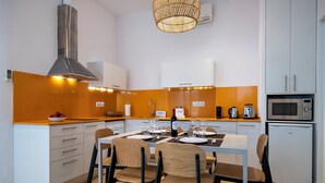 A modern kitchen with a dining area, featuring a stainless steel range hood, white cabinets, and a small refrigerator. - Verdi 12 - Habitat Apartments (Barcelona)