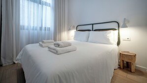A neatly made bed with white linens and towels, a bedside lamp, and a wooden stool. - Verdi 12 - Habitat Apartments (Barcelona)